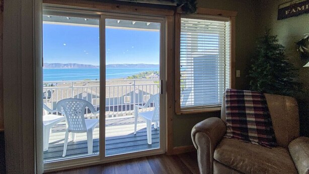 A room with a sliding glass door leading to a balcony with a view of the ocean and mountains.