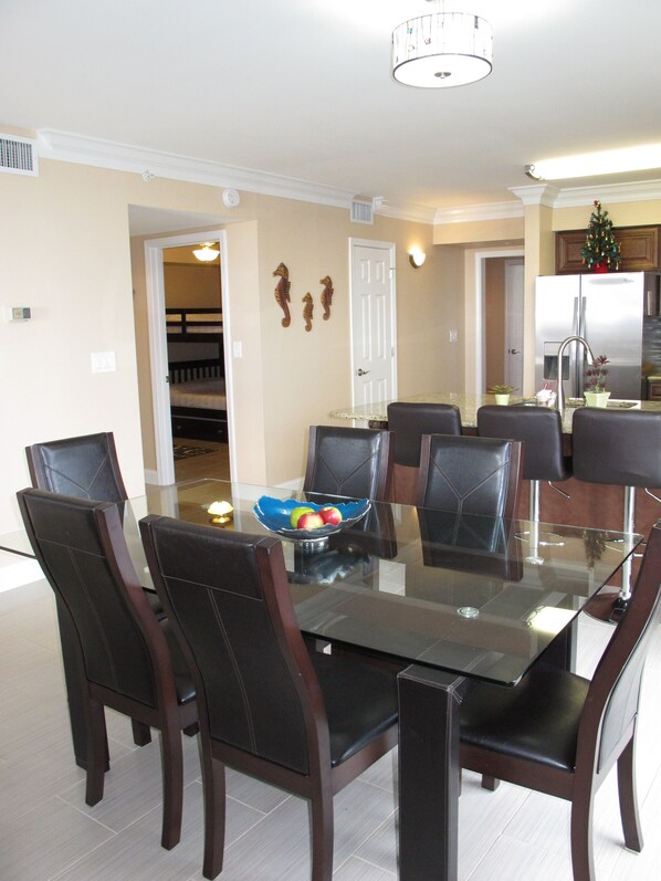 A dining area with a glass-top table, six dark brown chairs, and a bowl of fruit.