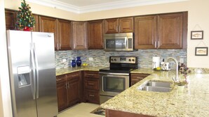 A modern kitchen with wooden cabinets, stainless steel appliances, a granite countertop, and a tiled backsplash. - Completely Remodeled Corner Unit With Amazing Gulf Views! (Destin)