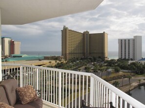 Un balcon offrant une vue sur un complexe hôtelier situé en bord de mer, comprenant des immeubles de grande hauteur et une étendue d’eau.