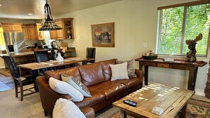 Un salon chaleureux avec un canapé en cuir marron, une table basse en bois et un coin repas comprenant une table et des chaises en bois.