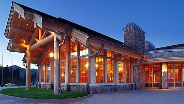 Un chalet doté d’une grande façade vitrée, d’un revêtement extérieur en pierre et d’un espace d’entrée abrité.