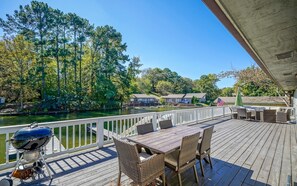 Une terrasse en bois avec un barbecue, des chaises en osier et une vue sur une rivière et des arbres.