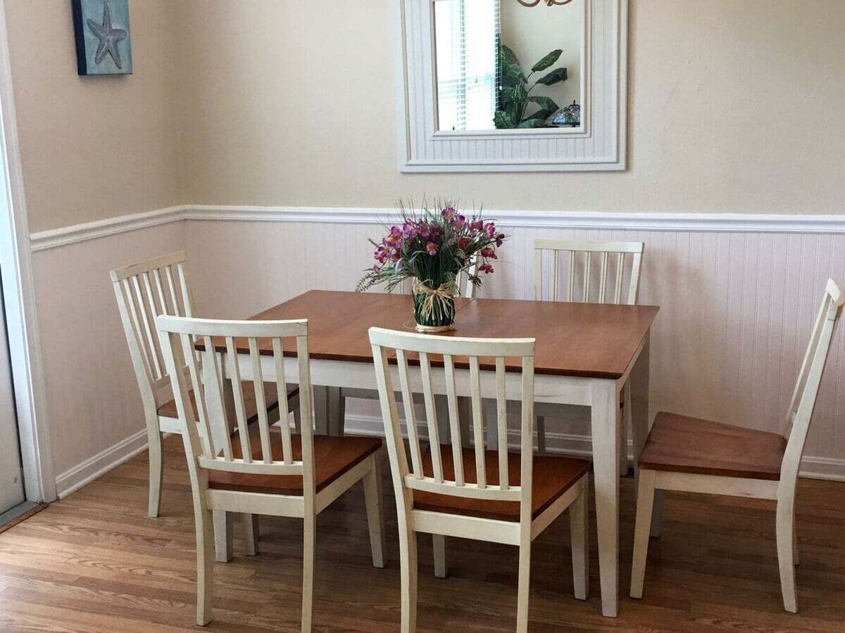 Una mesa de comedor con cuatro sillas, un florero con flores y un cuadro en la pared.