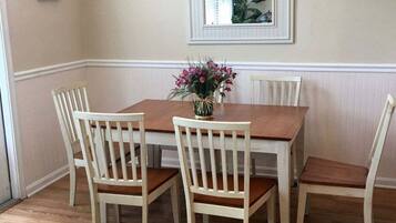 Una mesa de comedor con cuatro sillas, un florero con flores y un cuadro en la pared.