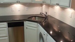 A compact kitchen with white cabinets, a stainless steel sink, a dishwasher, and a front-loading washing machine. - Great South End / Back Bay location, 1 bed condo near T station  (Boston)