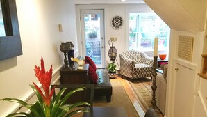 A modern living room with a dark wooden dining table, a black leather sofa, and a patterned armchair. A potted plant with red leaves is on the table, and a decorative wall piece is visible. - Great South End / Back Bay location, 1 bed condo near T station  (Boston)