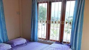 A bedroom with a bed, blue curtains, and a view of the outside. - Ban Sukjai Resort (Khao Kho)