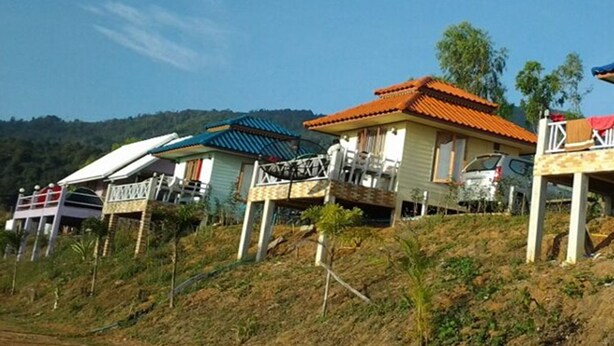 A row of houses with varying roof colors and designs, situated on a hillside with a clear sky. - Ban Sukjai Resort (Khao Kho)