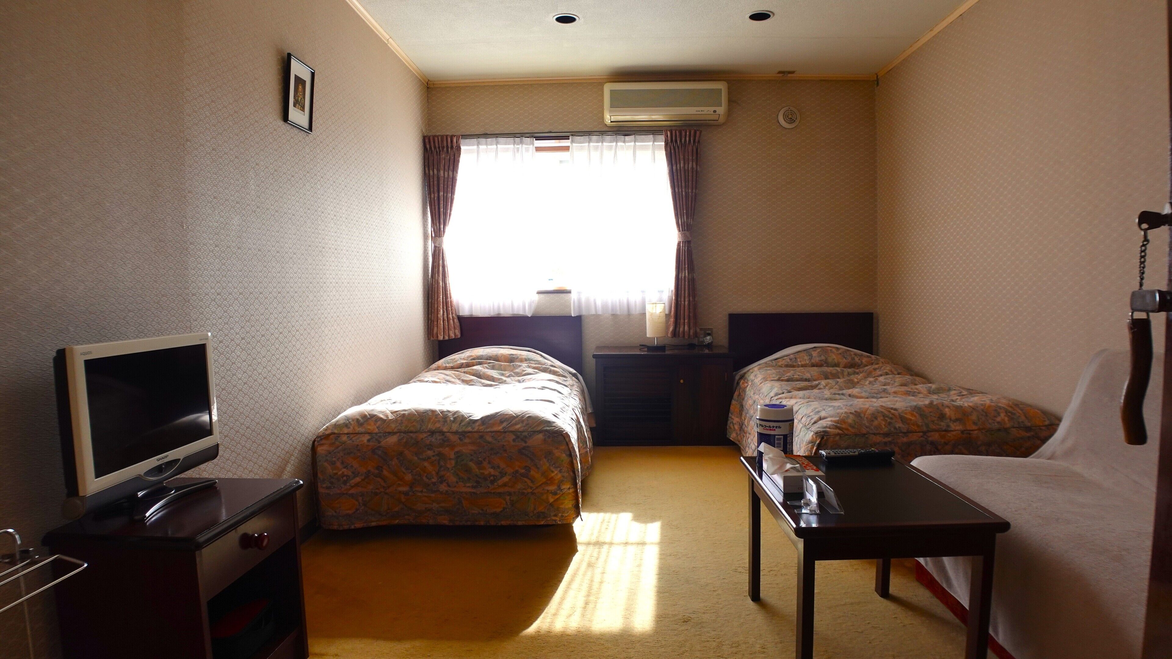 A hotel room with two beds, a TV, a desk, and a window with curtains.