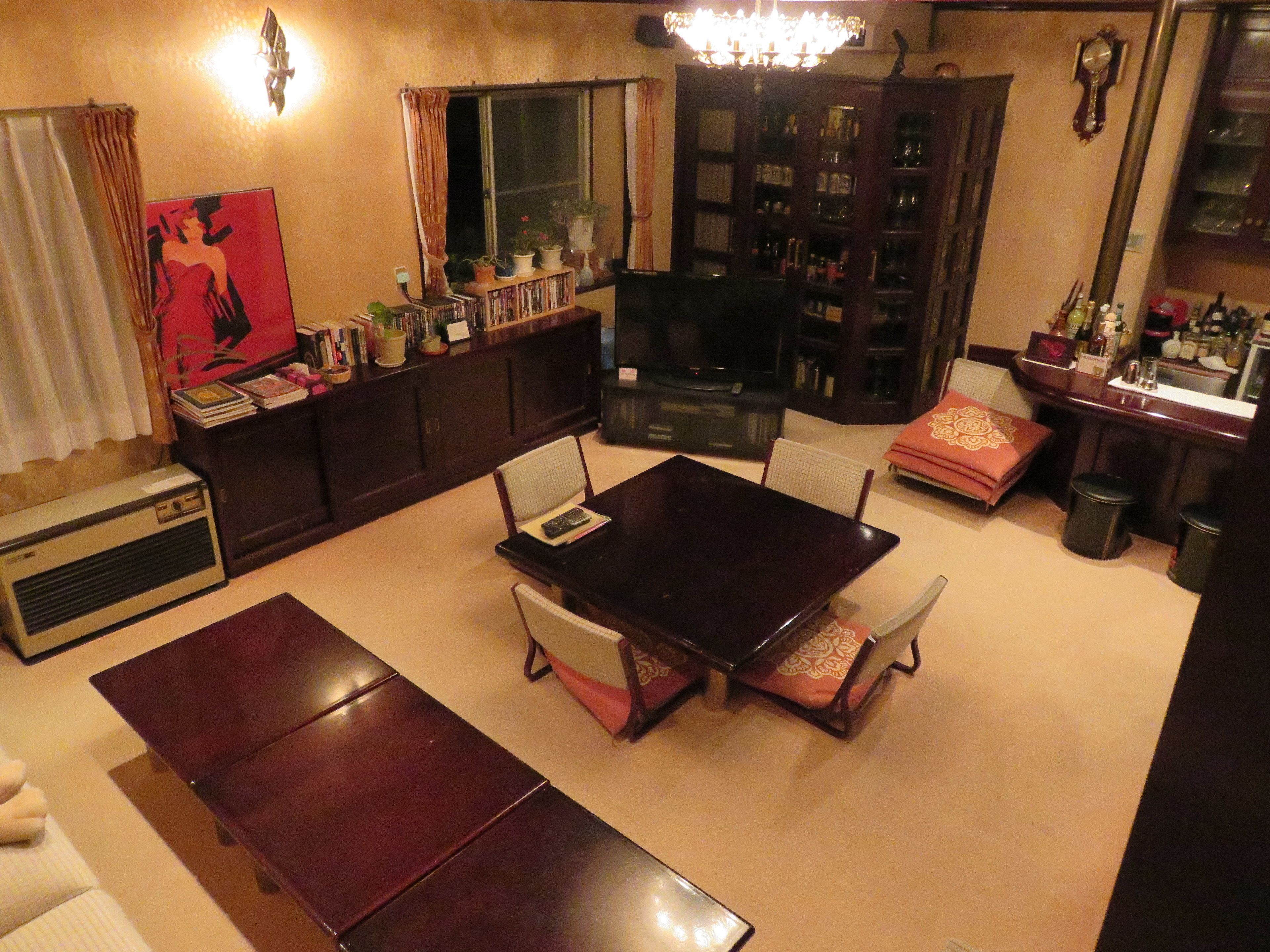 A living room with a dark wooden dining table, two chairs, a sofa, a TV, a bookshelf, and a decorative mirror.