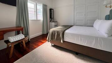 A bedroom with a bed, a desk, a chair, a wardrobe, and a window with curtains.