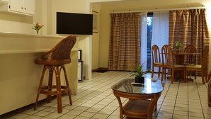 Een eetruimte met een tafel met glazen blad, rieten stoelen en een aan de muur bevestigde televisie.