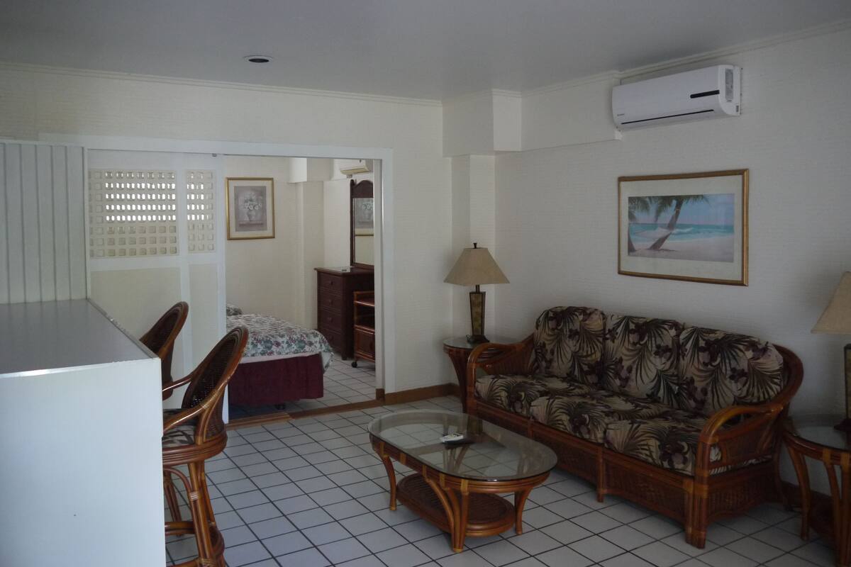 A living room with a sofa, a coffee table, a chair, a lamp, a picture frame, and an air conditioning unit.