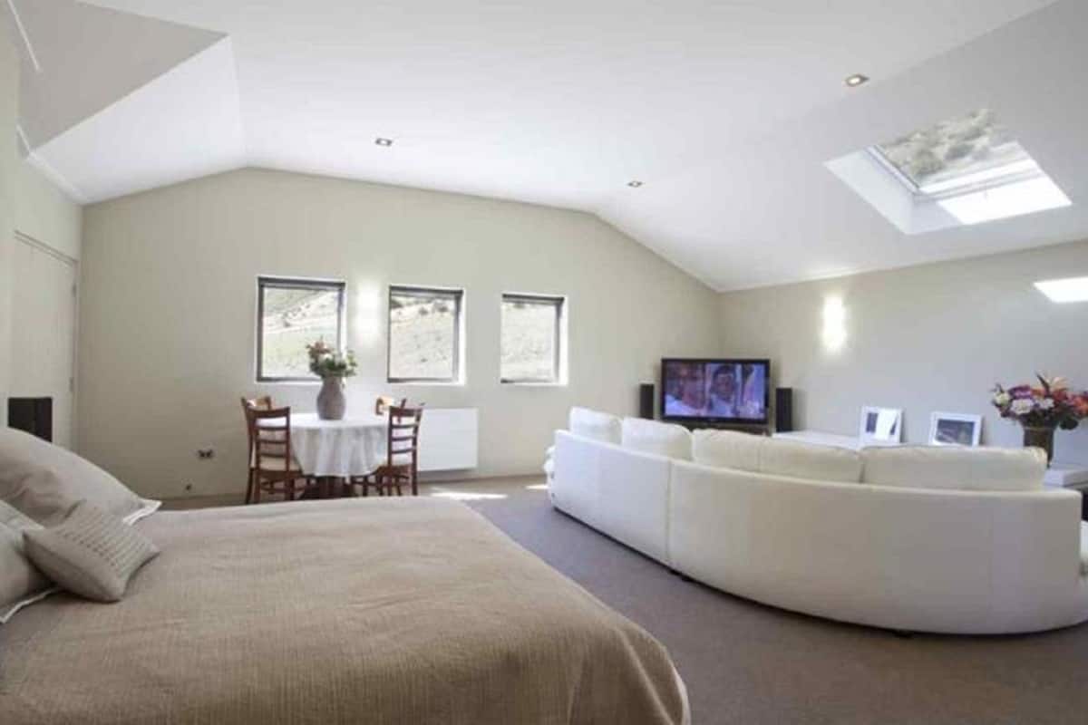 Um quarto espaçoso com uma cama grande, um sofá branco, um espaço de refeições e uma televisão.