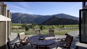 Une terrasse dotée d’une table ronde en bois et de quatre chaises, offrant une vue sur un vignoble et des montagnes.