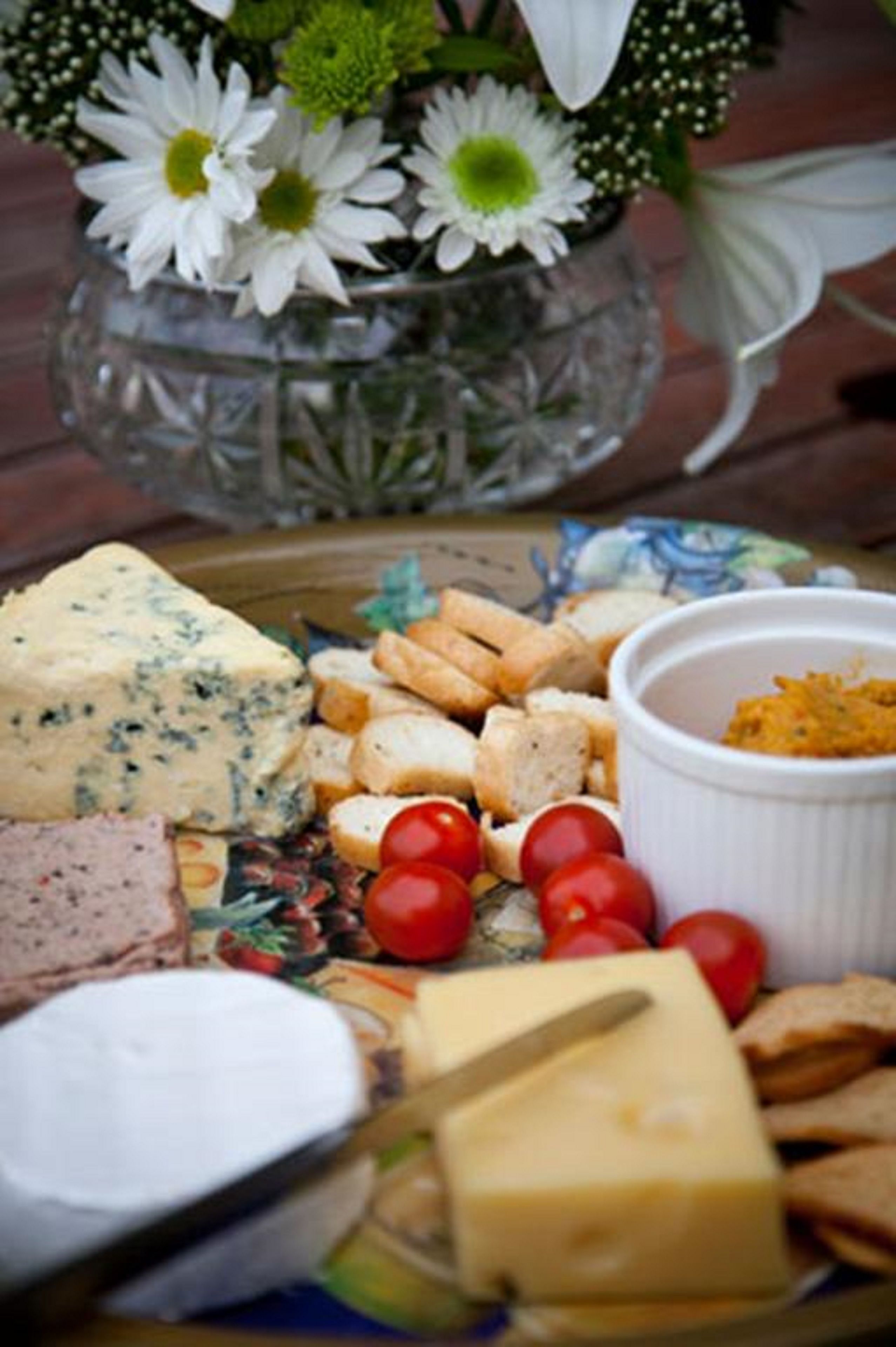 Una tabla de quesos con diferentes tipos de queso, galletas y tomates cherry sobre una mesa de madera.