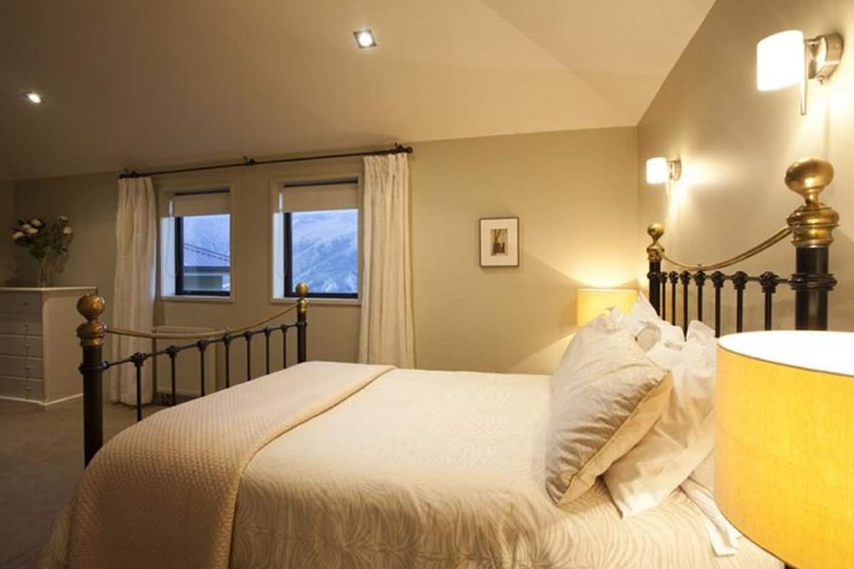 Um quarto com uma cama, abajur, janela com cortinas e um quadro na parede.