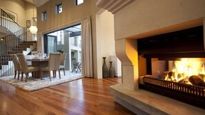 Un vaste salon doté d’une cheminée, de parquet, d’un coin repas avec des chaises et d’un escalier menant à l’étage supérieur.