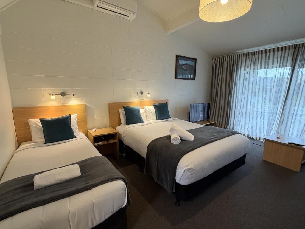 Ein Hotelzimmer mit zwei Betten, einem Fernseher, einem Fenster mit Vorhängen und einem Bild an der Wand.