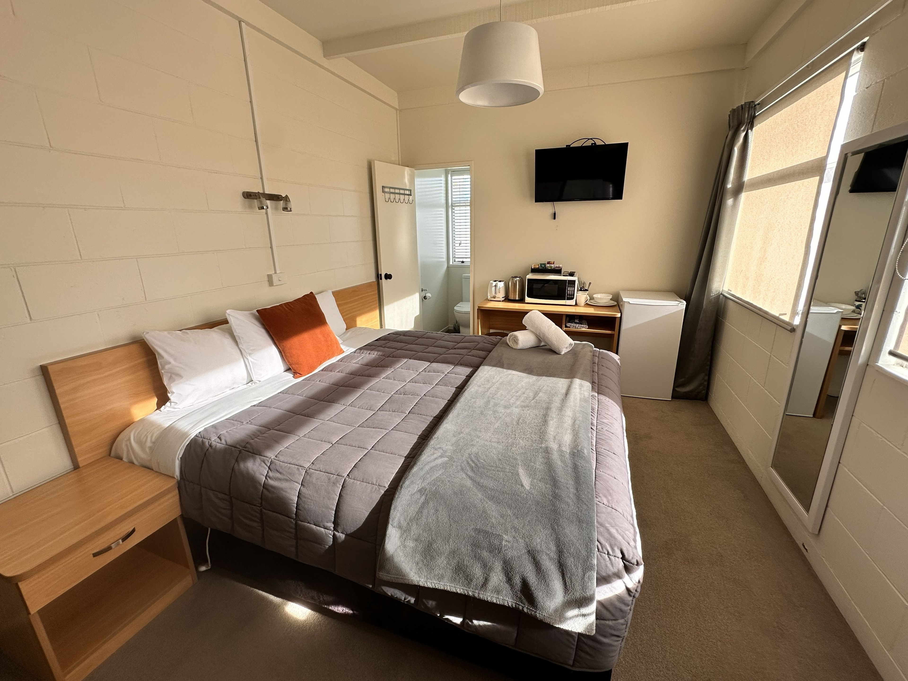 Un dormitorio ordenado con cama, mesita de noche y televisor sobre un mueble.