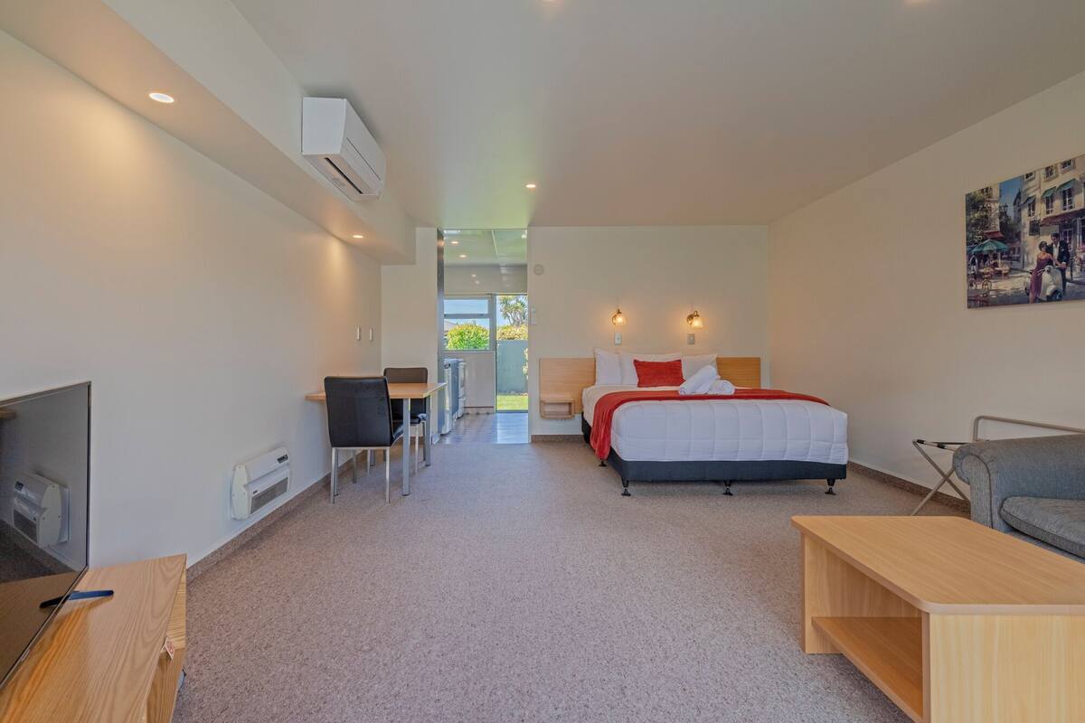 A modern hotel room with a bed, a desk, a chair, a TV, and a painting on the wall.