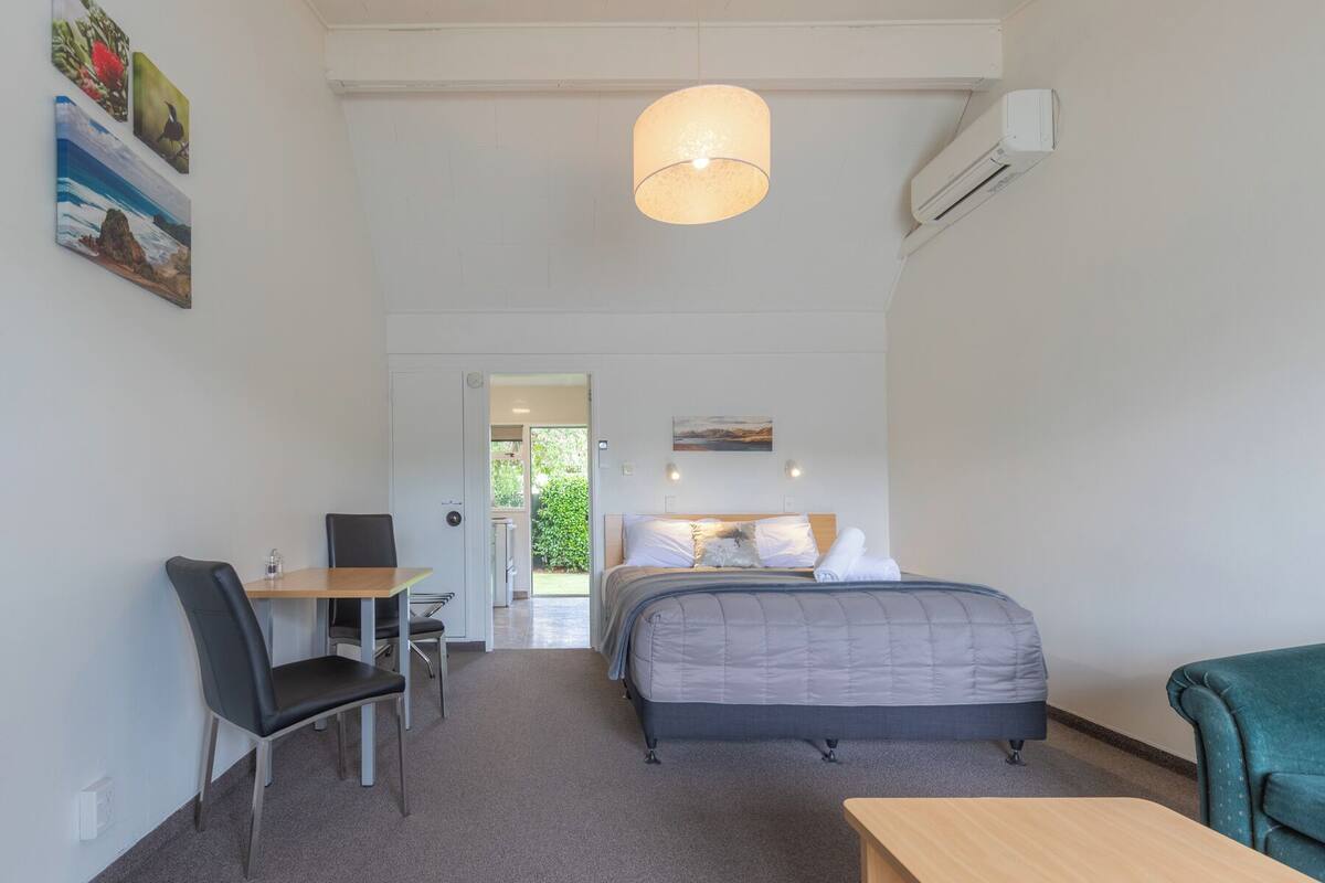 A bedroom with a bed, a desk, and a chair. There is a door leading to a balcony.