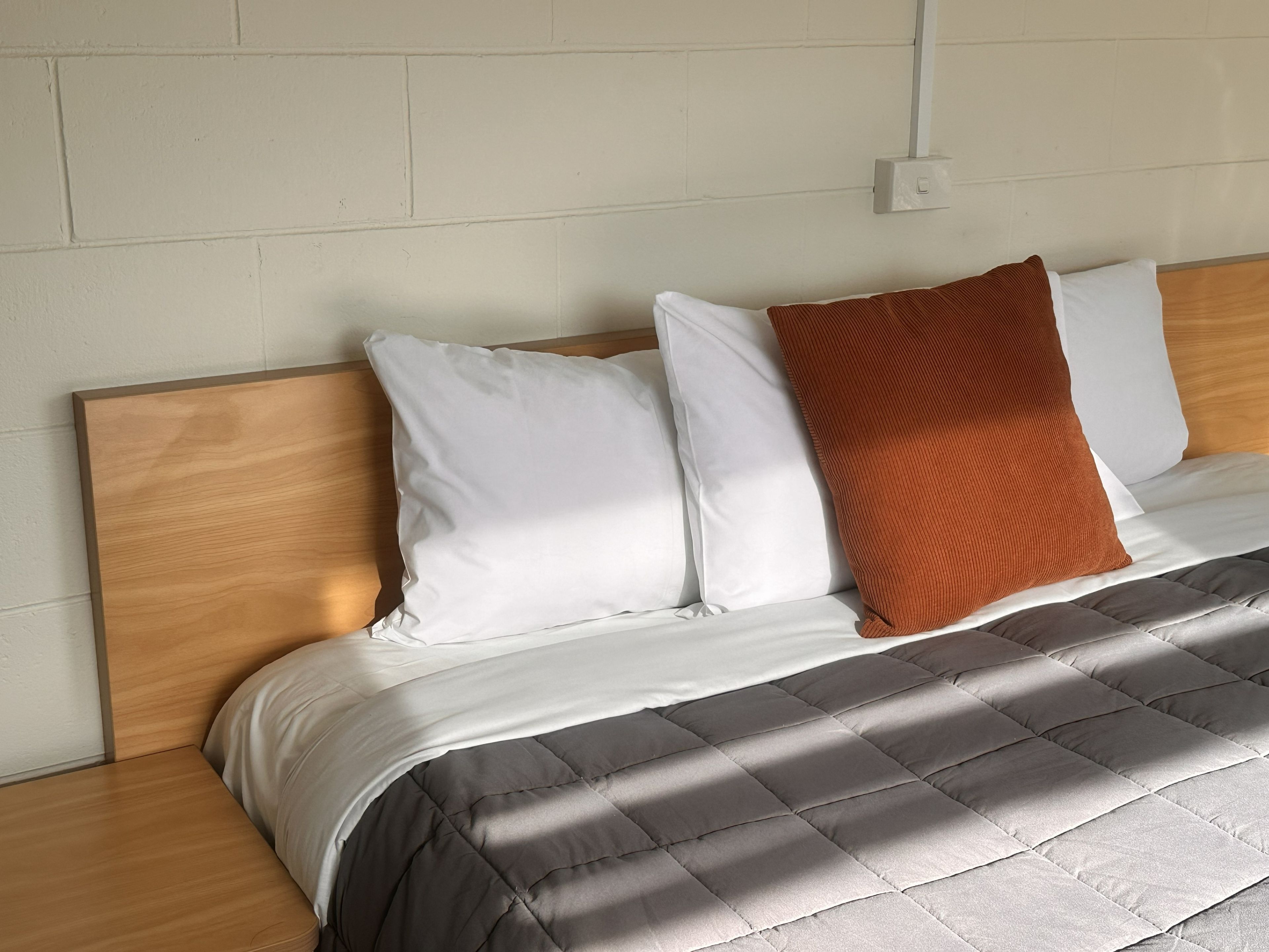 A bed with a wooden headboard, white pillows, and a brown accent pillow.