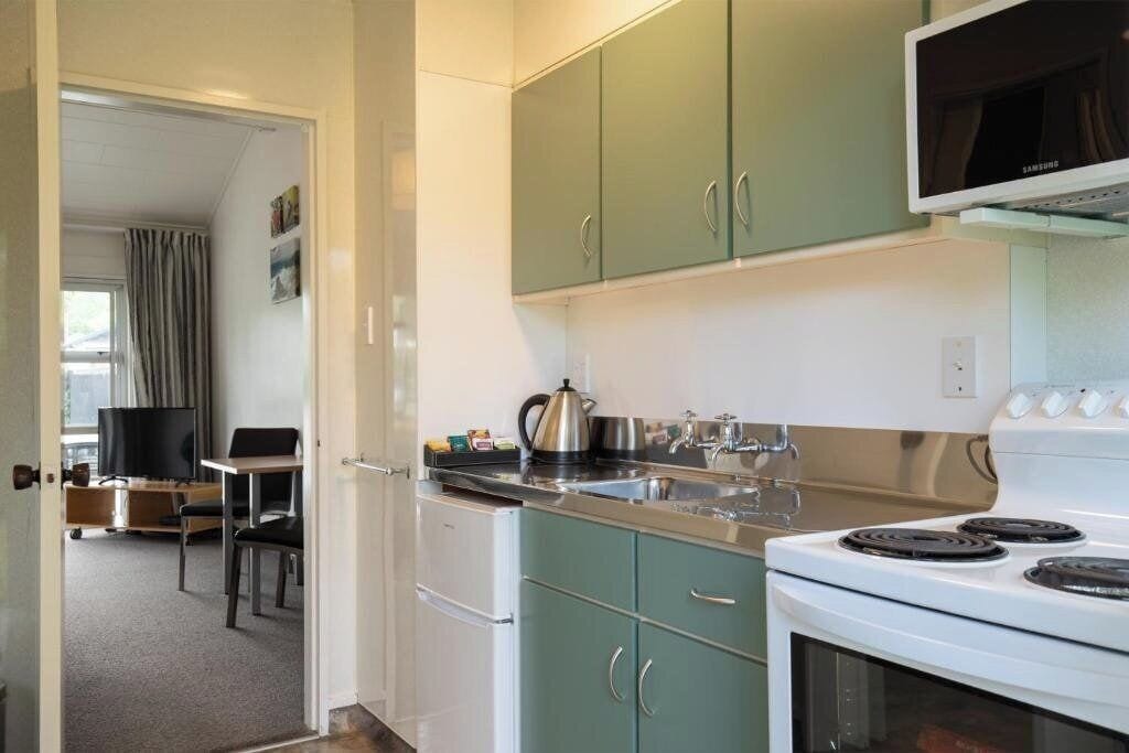 A compact kitchen with a stove, sink, and green cabinets.
