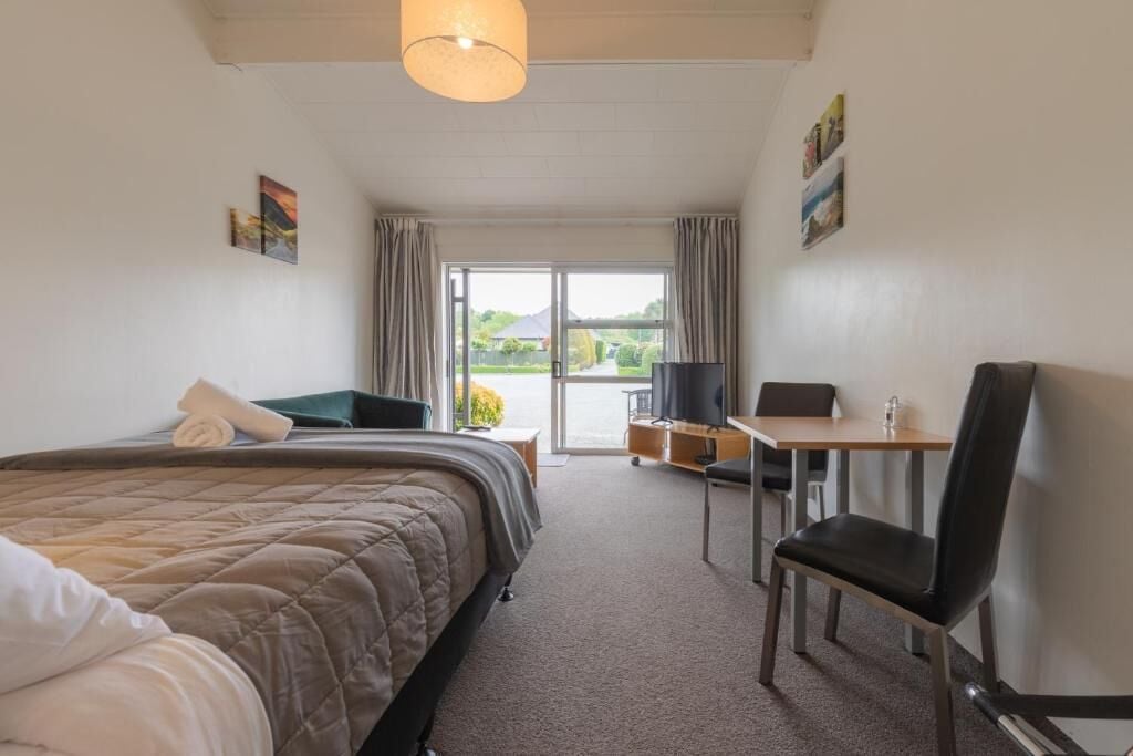 A hotel room with a bed, a desk, a chair, and a view of the outdoors.
