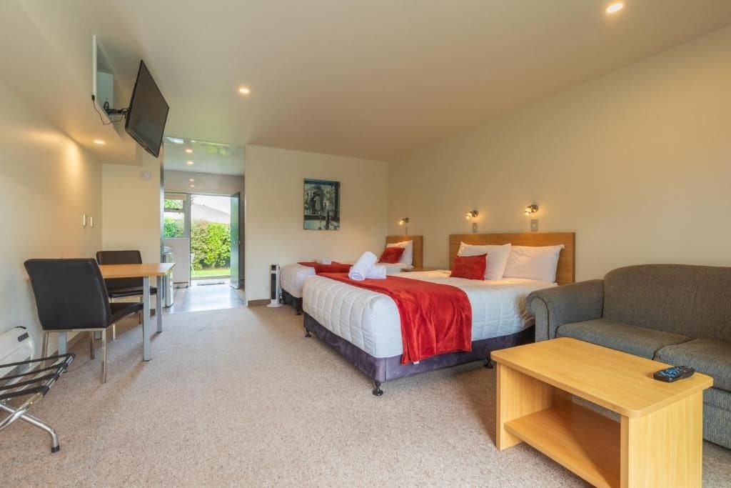 A hotel room with a bed, a desk, a chair, a sofa, and a television.