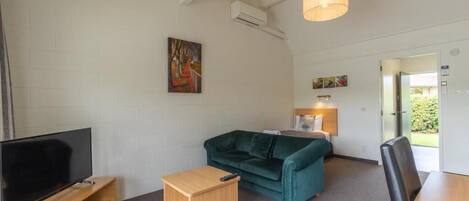A modern living room with a flat-screen TV, a green sofa, a small wooden side table, and a lamp.