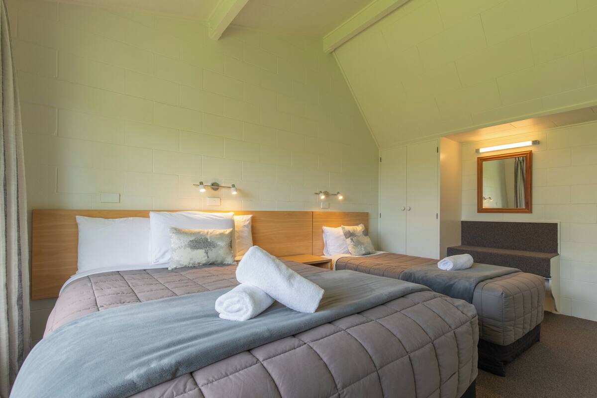 A hotel room with two beds, a wooden headboard, a mirror, and a light fixture above the beds.