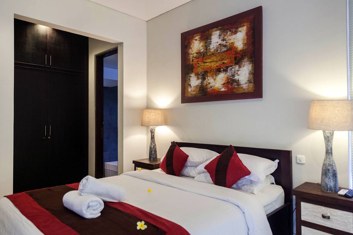 Une chambre d’hôtel avec un lit, deux tables de chevet avec des lampes, une armoire et un tableau au mur.