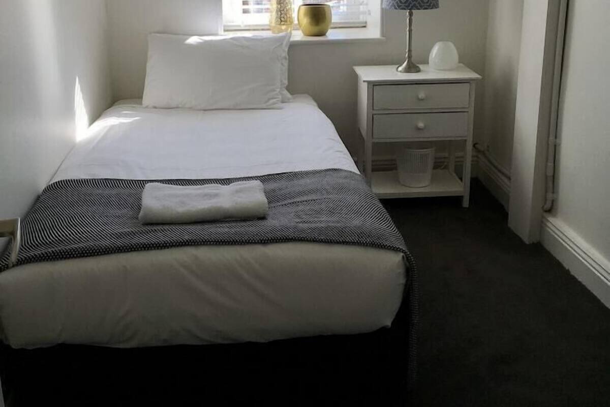 Une chambre à coucher avec un lit, une table de chevet, une lampe et une fenêtre avec des stores.