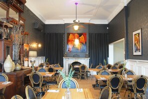 A dining area with wooden tables and chairs, a fireplace, and a ceiling fan. - Healesville Grand Hotel (Healesville)
