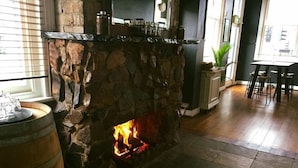 Una chimenea de piedra con fuego, un barril de madera y un área de comedor con sillas y una mesa.