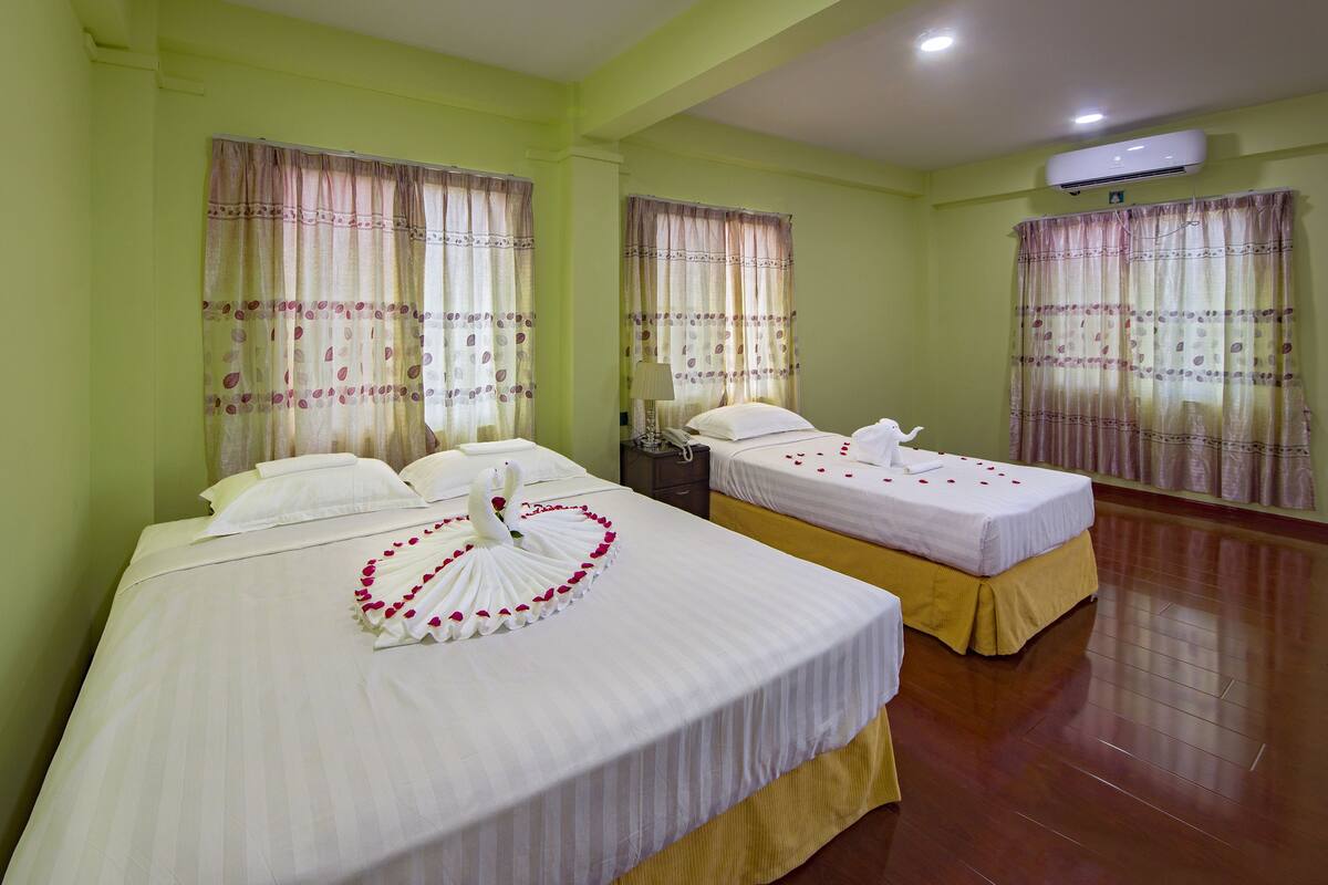 Une chambre d’hôtel avec deux lits, chacun recouvert d’une courtepointe blanche et agrémenté d’oreillers, et un cygne décoratif fait de pétales de rose placé sur le lit, au premier plan.