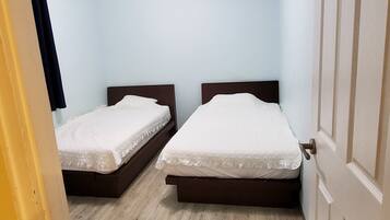 A room with two single beds, a wooden floor, a white air conditioning unit, and a door.