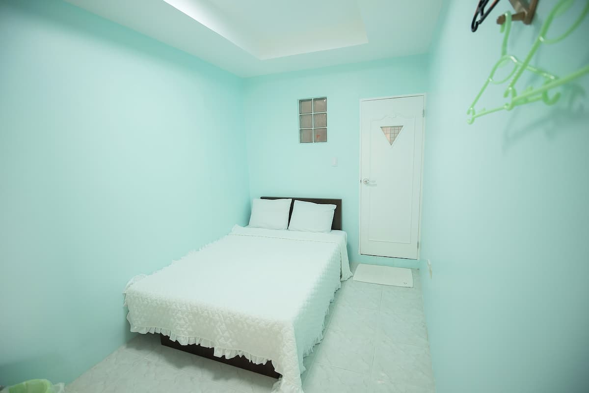 A room with a bed, a door, a small window, and a wall-mounted rack.