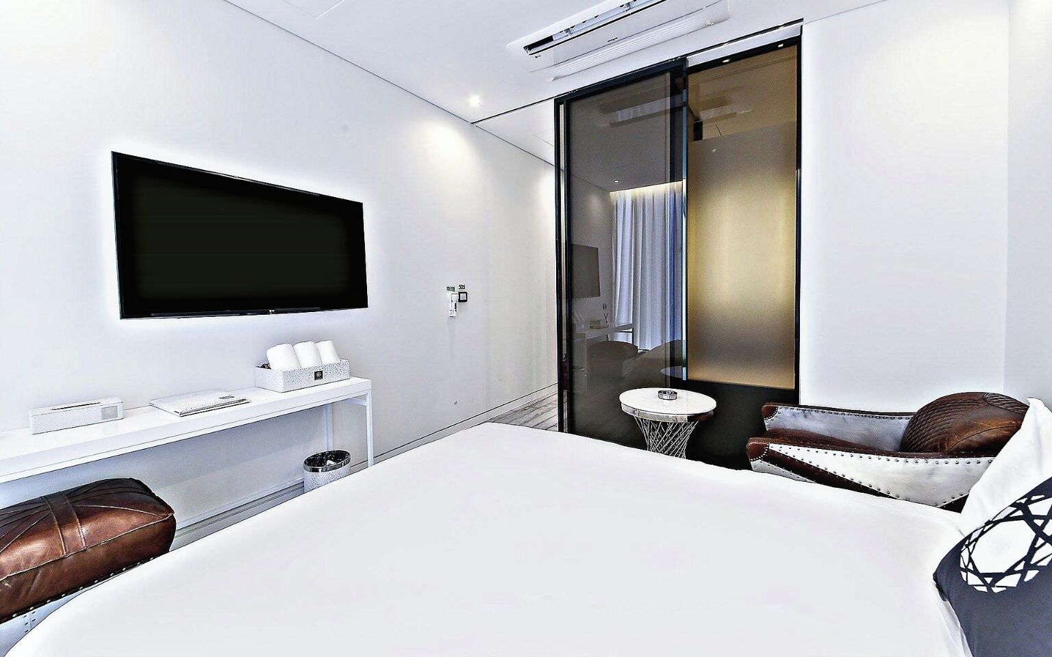 Ein modernes Hotelzimmer mit einem großen Bett, einem an der Wand montierten Fernseher, einem kleinen Tisch und einer Sitzecke mit Sessel und Sofa.