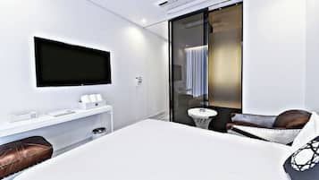 Ein modernes Hotelzimmer mit einem großen Bett, einem an der Wand montierten Fernseher, einem kleinen Tisch und einer Sitzecke mit Sessel und Sofa.
