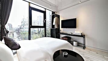 A modern hotel room with a large bed, a TV, a desk, and a view of the city.