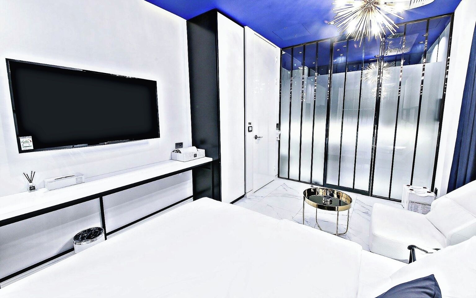 Een moderne woonkamer met een flatscreen televisie, een witte bank, een salontafel en een glazen scheidingswand met verticale jaloezieën.
