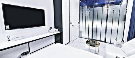 Een moderne woonkamer met een flatscreen televisie, een witte bank, een salontafel en een glazen scheidingswand met verticale jaloezieën.