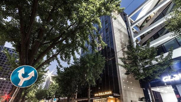 A modern hotel with a prominent entrance, a visible sign for 'Hotel Cullinan', and a street sign indicating a roundabout ahead. - Hotel Cullinan (Seoul)