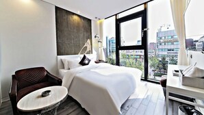 A modern hotel room with a large bed, a seating area with a chair and a small table, and a view of the city through large windows. - Hotel Cullinan (Seoul)