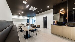 A modern dining area with a long bench, multiple tables, chairs, and a kitchen counter with appliances. - Hotel Cullinan (Seoul)