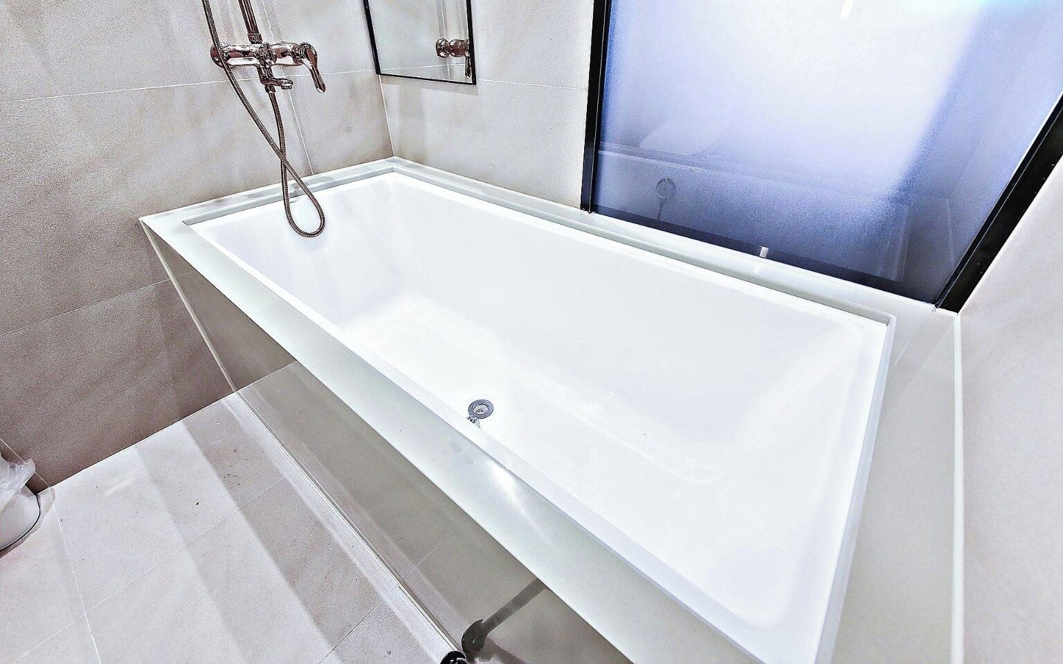 Un baño moderno con una bañera blanca, una cabina de ducha de vidrio y desagüe visible.