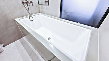 Un baño moderno con una bañera blanca, una cabina de ducha de vidrio y desagüe visible.